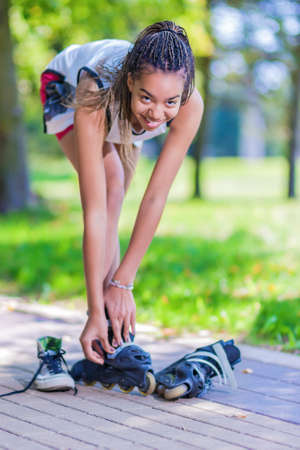 Teenager Lifestyle Concepts. African American Teenage Girl Puts On Roller Skates in Park Outdoors.Vertical Imageの写真素材