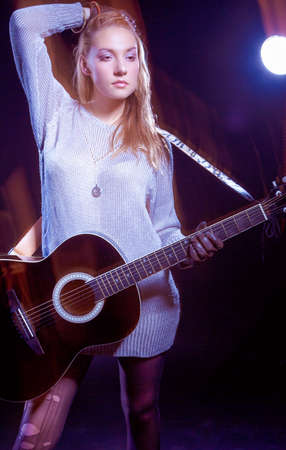 Portrait of Caucasian Expressive Blond Female Posing with Guitar Against Black. Combination of Flash...