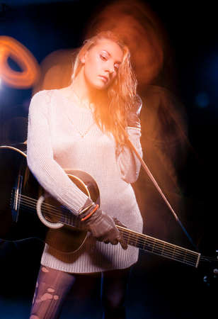 Portrait of Caucasian Expressive Blond Female Posing with Guitar Against Black. Combination of Flash...