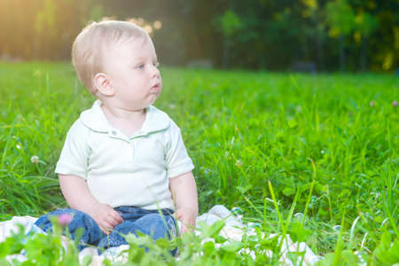 Portrait of Little Cute Caucasian Boy Sitting Alone on Grass Outdoors. Horizontal Imageの写真素材