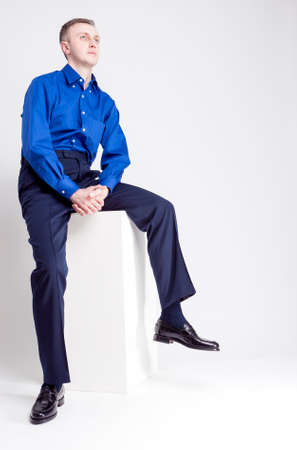 Young Adults Concepts. Full Length Portrait of Handsome Caucasian Man With Folded Hands Posing in Blue Shirt and Dark Blue Chinos Against White Background. Vertical Image Compositionの写真素材