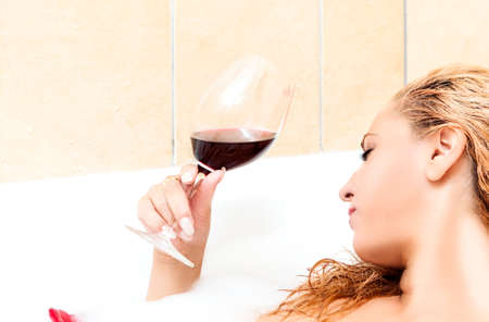 Dreaming Caucasian Female Blond in Bath Relaxing with Glass of Red Wine.Horizontal Image Orientationの写真素材