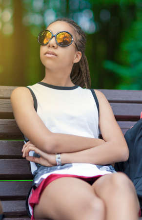Portrait of African American Teenage Girl With Long Dreadlocks Posing in Park Outdoors in Sunglasses. Vertical Image Compositionの写真素材
