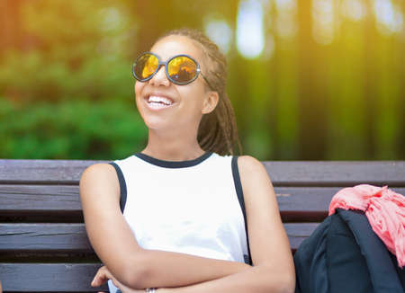 Happy and Smiling African American Teenage Girl With Long Dreadlocks Posing in Park Outdoors in Sunglasses. Horizontal Image Compositionの写真素材