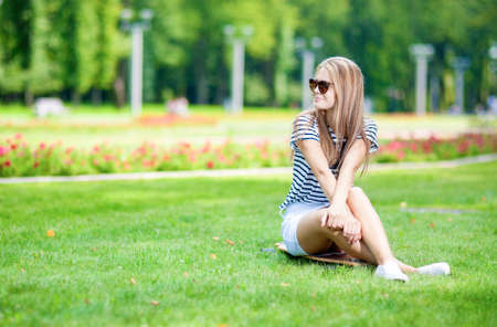 Portrait of Cute and Positive Caucasian Blond Teenager Girl Posing On Longboard in Green Summer Park.Horizontal Imageの写真素材