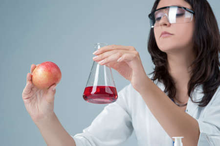 Medicine and Research Ideas. Laboratory Female Staff Dealing with Apple Specimen and Test Liquid in Flask.Horizontal Imageの写真素材