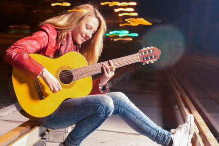 Youth Lifestyle Ideas and Concepts. Young smiling Caucasian Blond Woman Playing The Guitar Outdoors...