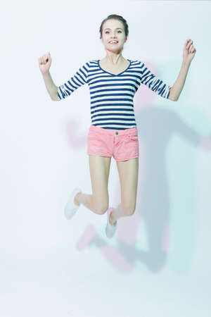 Portrait of Exclaiming Happy Caucasian Girl in Shorts Jumping Against White Background. Vertical Imageの写真素材