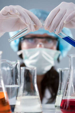 Researching and Science Concepts. Female Laboratory Staff in Facial Mask And Protective Gloves Conducting Experiment with Flasks in Lab. Vertical Image Compositionの写真素材