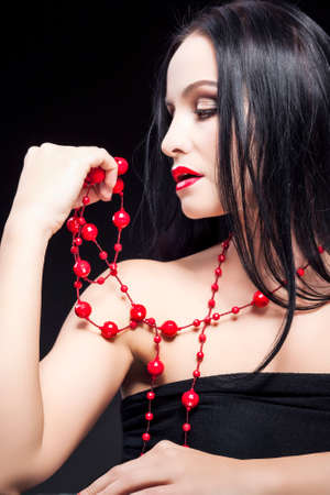 Portrait of Sensual Caucasian Brunette Woman Posing With Long Red Beads Against Black Background.Vertical imageの写真素材