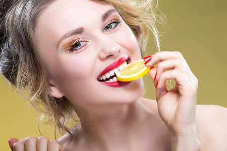 Sexy Fruit Series. Closeup Portrait of Cute Funny Naked Caucasian Girl Holding Lemon Slice In Front of Her Mouth. Posing Against Yellow. Horizontal Image Compositionの写真素材