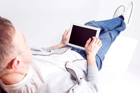 Technology Ideas and Concepts. Portrait of Relaxed Caucasian Man Working with Tablet Computer while Lying on Floor with Legs Lifted on Box in Front. Horizontal Image Orientationの写真素材