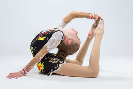 Young Caucasian Female Rhythmic Gymnast Athlete In Professional Competitive Suit Doing Backbend Stretching Exercise Pose in Studio Against Whiteの写真素材