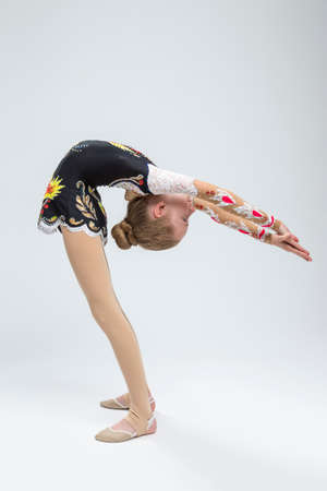 Young Caucasian Female Rhythmic Gymnast Athlete In Professional Competitive Suit Doing Backbend Stretching Exercise While Posing in Studioの写真素材