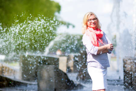 Middle Aged Females Concepts. Portrait of Mature Middle Aged smiling Blond Woman Wearing Spectacles Posing Outdoors in Park.Hands Folded in Front. Horizontal Image Compositionの写真素材