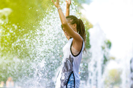 Portrait of Smiling Funny African American Teenager Girl with Dreadlocks Enjoying in Fountain Outdoorsの写真素材