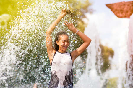 Teenager Ideas. Happy Smiling African American Teenage Girl with Dreadlocks and Sunglasses Having Fun Time in Fountain Outdoors.Horizontal Image Compositionの写真素材