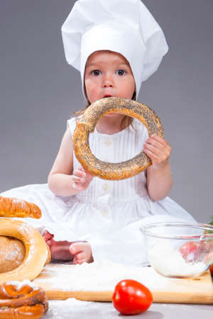 Food Concepts and Ideas. Little Caucasian Girl In Cook Uniform Posing With Doughnut Bread Roll In Studio Environment.Vertical Image Compositionの写真素材