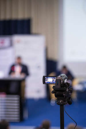 Back View of Compact Videocamera. Positioned Against Blurred Background with Host Speaking on stage....
