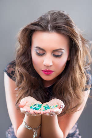 Portrait of Pretty Smiling Caucasian Brunette Woman Holding New Year Confetti in Hands and Blowing Around.Against Gray Background.Vertical Imageの写真素材