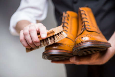Footwear Concepts and Ideas. Closeup of Hands of Man Cleaning Premium Derby Boots With Variety of Brush.Horizontal Imageの写真素材