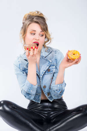 Food Ideas and Concepts. Portrait of Young Surprised Caucasian Blond Girl Eating Two Big Doughnuts in Hands. Posing Against White Background.Vertical Compositionの写真素材