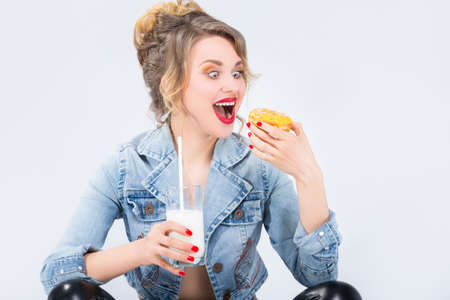 Food Ideas and Concepts. Young Caucasian Blond Girl Having Fun with Cup of MIlk and Donut Bagel.Eating Pastry and Posing Against White Background.Horizontal Imageの写真素材