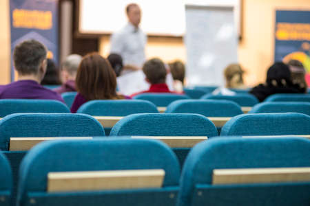 Meetings Concepts. People Listening to a Male Presenter Holding a Conference In Front of a Group of Listeneres in a Congress Hall. Standing in Front of The Big Screen.Horizontal Image compositionの写真素材
