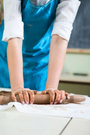 Extreme Closeup of Hands of Female Professional in Apron Rolling Out a Piece of Clay with Rolling Pin in Workshop.Vertical Imageの写真素材