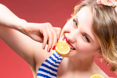 Fruit Series. Portrait of Passionate Caucasian Blond Biting Lemon Slice. Against Red Background.Horizontal Imageの写真素材