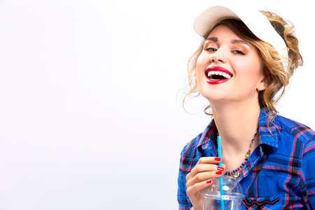 Happy Lifestyle Concepts. Portrait of Upbeat Smiling Caucasian Blond Woman in Checked Shirt Drinking Blue Juice. Wearing Sun Visor. Horizontal Image Compositionの写真素材