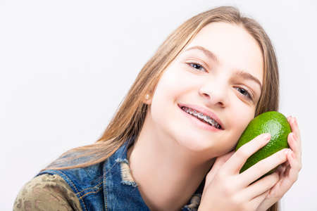 Portrait of Smiling Caucasian Female Teenager With Teeth Braces. Posing with Long Green Avocado...