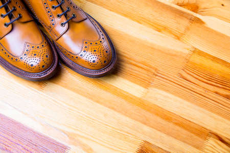 Footwear Ideas and Concepts. Closeup of Tips of Male's Brooge Boots in Tan Color. Standing On Wooden Yellowish Background.Horizontal Imageの写真素材