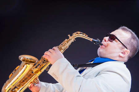 Music Concepts. Expressive Mature Playing Saxophonist Posing In Sunglasses With Sax. Against Black...