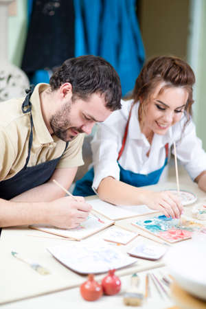 Pottering Ideas. Caucasian Ceramists Painting and Glazing Clay Crafts Together in Workshop Using...