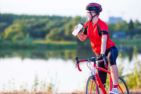 Male Cyclist Having a Rest. Drinking Refreshing Liquid from the Bottle. Shot Made Outdoors. Horizontal Imageの写真素材
