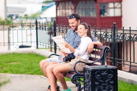 Young Positive Caucasian Couple Travelling Across the City. Checking Route Using City Map Outdoors. Loughing Together Embraced. Horizontal Imageの写真素材
