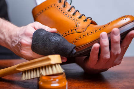Luxury Footwear Ideas. Closeup of Mans Hands with Cleaning Cloth Used for Polishing and Creaming Tan High Derby Boots. Studio Shot.Horizontal Compositionの写真素材
