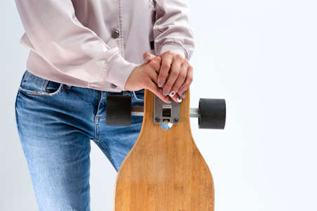 Closeup of hands of Caucasian Girl in Pink Hoodie Holding Longboard In Front. Against White.Vertical...
