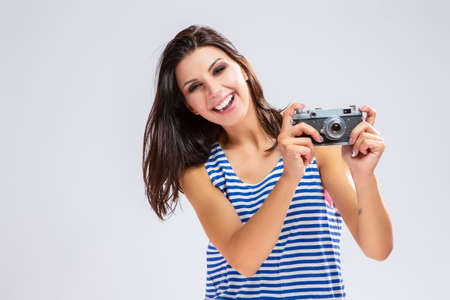 Portrait of Happy Caucasian Brunette Girl in Sweatshirt making Photos with Old Fashioned Film Camera. Posing Against White. Horizontal Image Compositionの写真素材