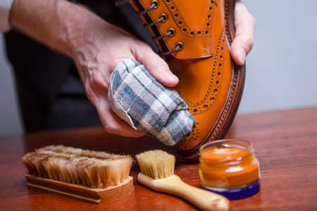 Mens Footwear Care Ideas. Closeup of Mans Hands with Cleaning Cloth Used for Polishing Tan High Derby Boots. Studio Shot. Horizontal Image Compositionの写真素材