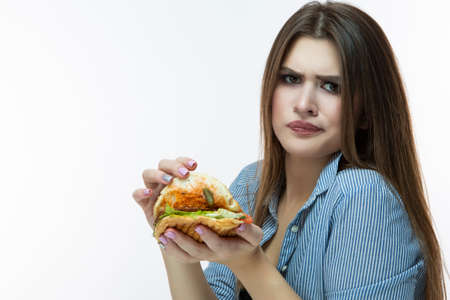 Fastfood Eating Concept. Young Caucasian Female Eating Burger With Displeasing facial Expression in...