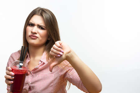 Portrait of Unhappy Caucasian Brunette Woman  Holding Red Fresh Smoothie Juice.Thumbs Down Sign.Horizontal imageの写真素材