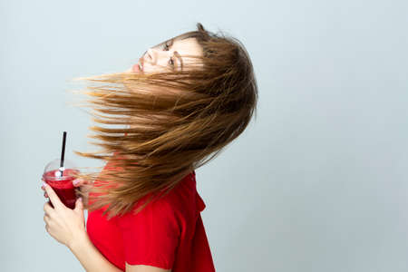 Positive Caucasian Female Dancing with Cup of Red Smoothie Juice Mix. Posing in Red Dress Over...