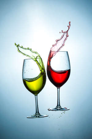 Two Types of Colorful Red and Light Yellow Wine Splashes Poured Out from Glasses Against Bluish Background. Short Flash Duration for Freezing Motion Used. Vertical Image Orientationの写真素材