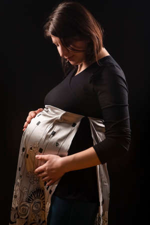 Portrait of Tranquil Pregnant caucasian Woman in Supporting Dress. Against Black Background.Horizontal imageの写真素材