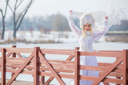 Woman Winter Fashion. Portrait of Sensual Caucasian Blond in Knitted White Dress and Kerchief with Fur Kokoshnik.Posing on Bridge in Winter.Horizontal Image Compositionの写真素材