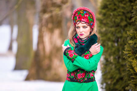 Sensual Caucasian Blond Girl in Fashionable Green Dress and Kokoshnik with Flowery Pattern and Beads. Posing In Winter Snowy Park Outdoors. Horizontal Image Orienationの写真素材