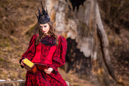 Art Photography. Mysterious Fairy Medieval Queen in Red Dress and Spiky Black Crown Posing With...
