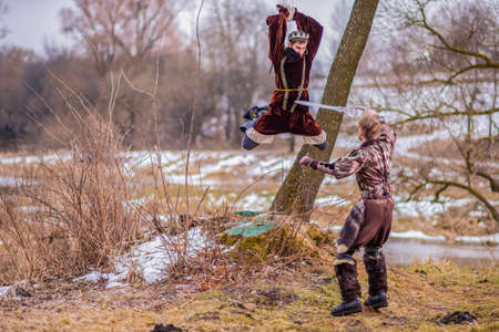 Costume Play Art Photography. Two Knights Fighting on Swords in Forest Outdoors Against River On...